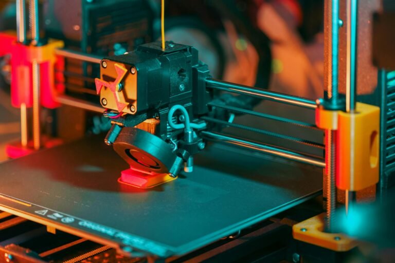 Close-up of a 3D printer's extruder and print bed, showcasing the intricate mechanics and vibrant lighting, highlighting the technology used in additive manufacturing.