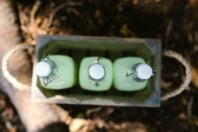 Three glass bottles with white caps containing a light green liquid, arranged in a wooden crate, set against a natural background with leaves and earth.