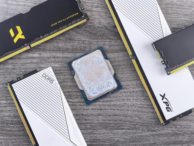 Close-up image of computer hardware components featuring DDR5 RAM modules from Goodram and XPG, along with a CPU in the center. The image highlights the sleek design and branding of the RAM sticks against a textured wooden background, showcasing essential elements for high-performance computing.