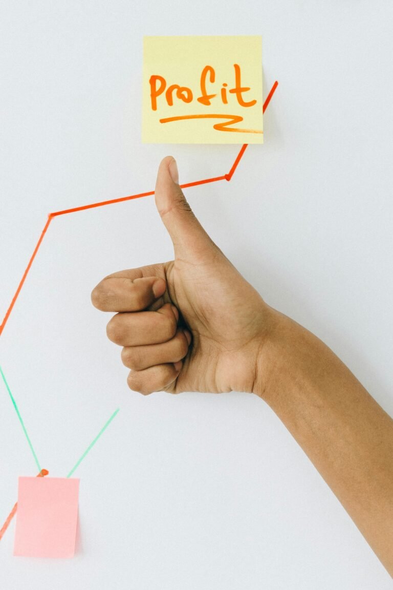 Hand giving a thumbs up next to a sticky note labeled "Profit," with an upward trending graph drawn on a whiteboard, symbolizing business success and growth.