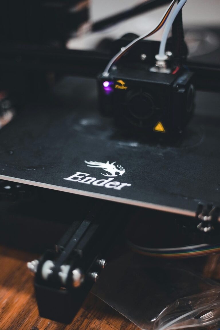 Close-up of an Ender 3D printer showcasing the print bed with the Ender logo, highlighting the printer's nozzle and wiring setup for filament extrusion, on a wooden surface.