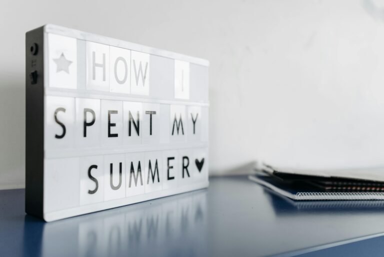 Lightbox display with the phrase "How I Spent My Summer" on a blue tabletop, accompanied by notebooks and stationery, symbolizing summer reflections and activities.